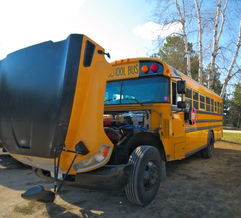 Yellow school bus parked with its hood tilted open for engine work
