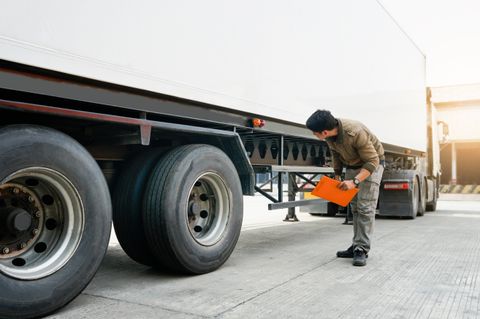 Inspector with a clipboard checking the underside of a semi trailer