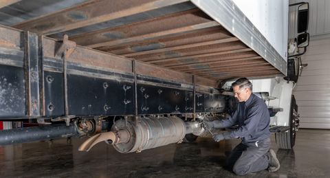 Technician kneeling under a medium-duty truck working on the DPF and aftertreatment canister