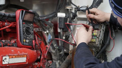 Technician probing a fuse panel with a multimeter during electrical diagnostics on a heavy-duty truck