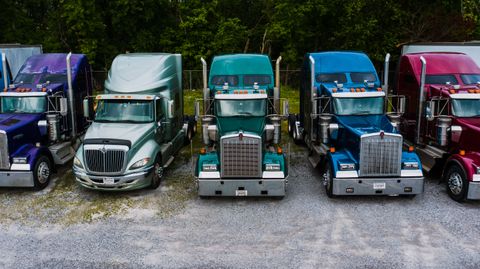 Row of parked semi tractors lined up on a gravel yard