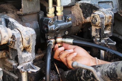 Hands connecting a hydraulic hose on a piece of heavy equipment
