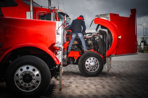 Technician leaning into the open engine bay of a red semi tractor
