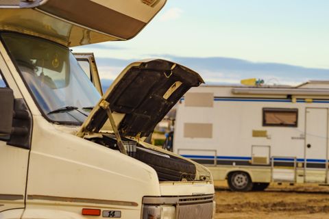 Motorhome with its hood raised beside a parked travel trailer