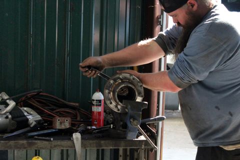 Technician at a bench in the ACME Precision Diesel shop turning a wrench on a wheel hub held in a vise