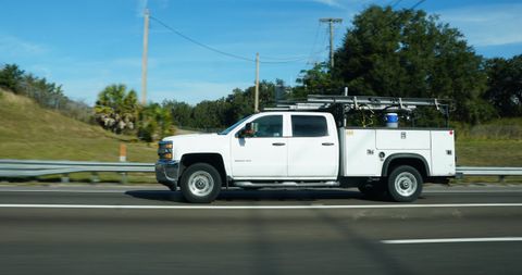 White crew-cab service truck with a utility body and ladder rack driving on a highway