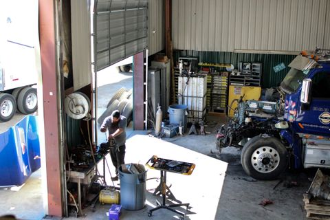 Technician working at a bench inside the ACME Precision Diesel shop with a blue semi tractor torn down for engine work beside him