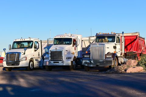 Three semi tractors parked side by side on a fleet yard in morning light
